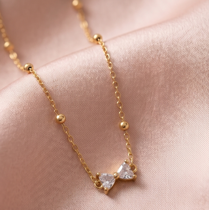 Gold necklace with a diamond pendant on a soft pink fabric background