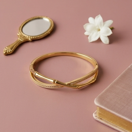 Gold bracelet with a small mirror, flower, and notebook on a pink background