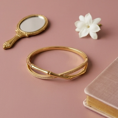 Gold bracelet with a small mirror, flower, and notebook on a pink background