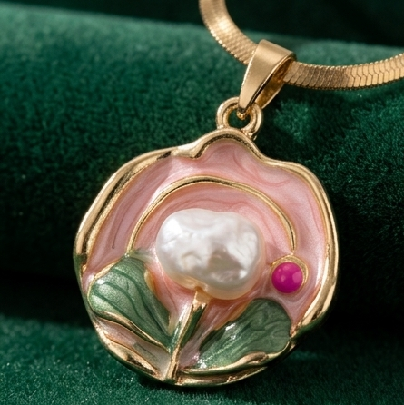 Gold pendant with a pearl and pink stone on a green fabric background