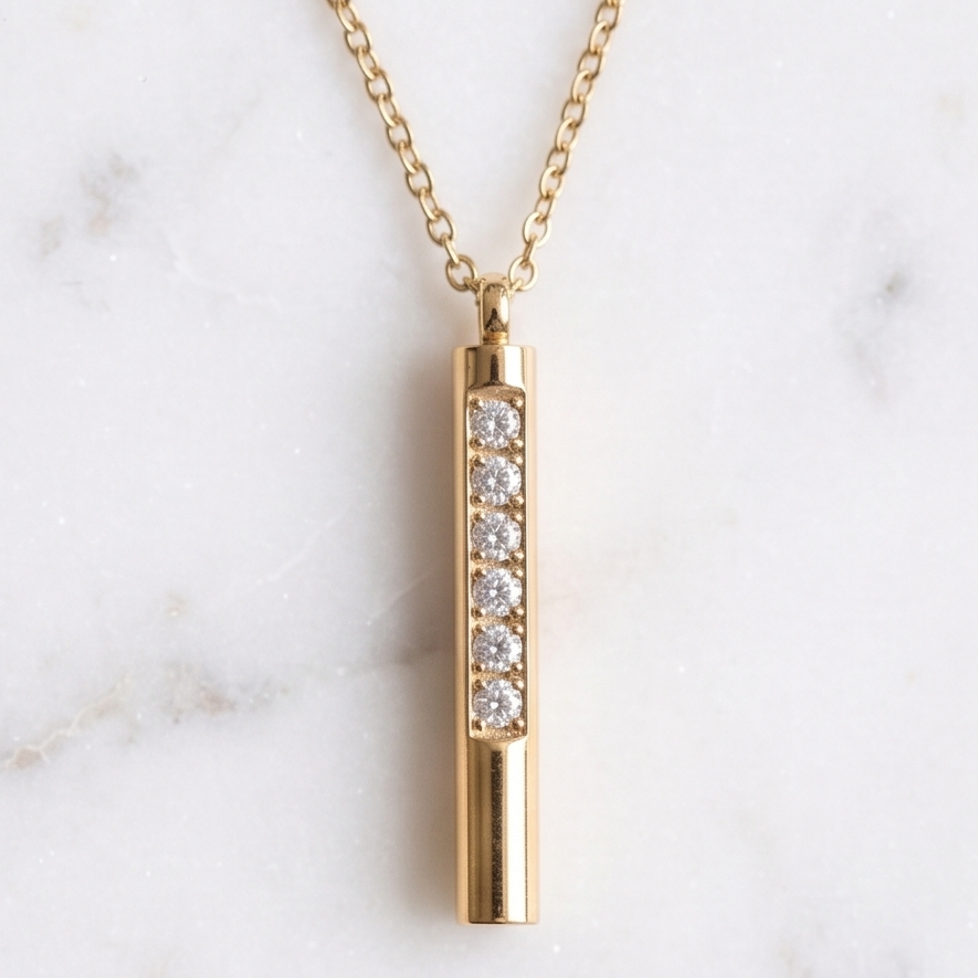 Gold necklace with a cylindrical pendant featuring embedded diamonds on a marble background