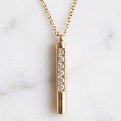 Gold necklace with a cylindrical pendant featuring embedded diamonds on a marble background