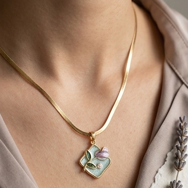 Gold necklace with a floral pendant worn by a person, with a blurred background.