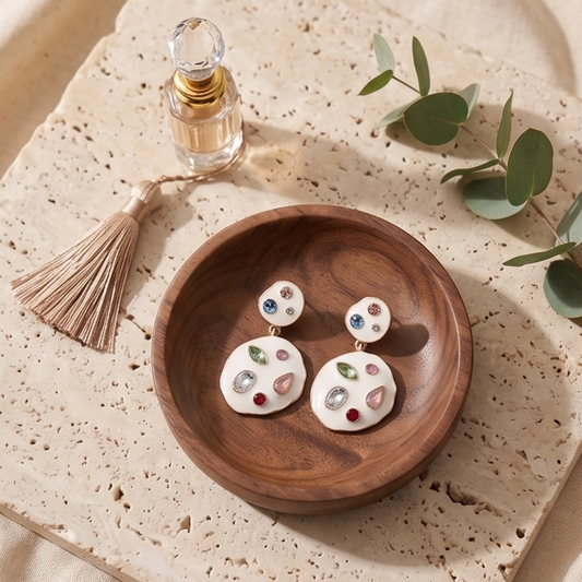 Wooden dish with earrings on a textured surface with a small plant and perfume bottle.