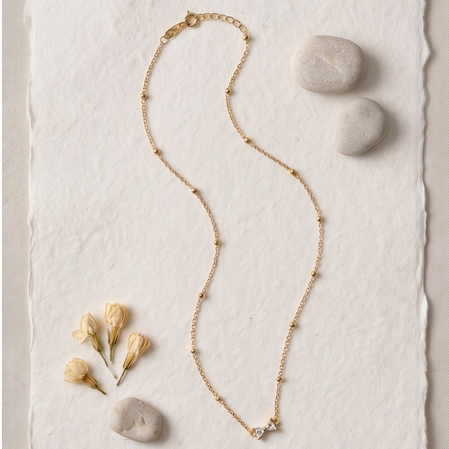 Gold necklace on a textured white surface with stones and flowers