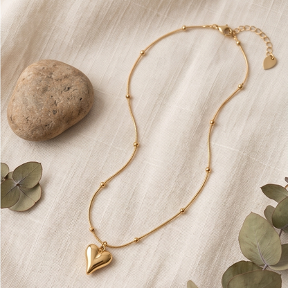 Gold necklace with heart pendants on a neutral background with leaves and a rock