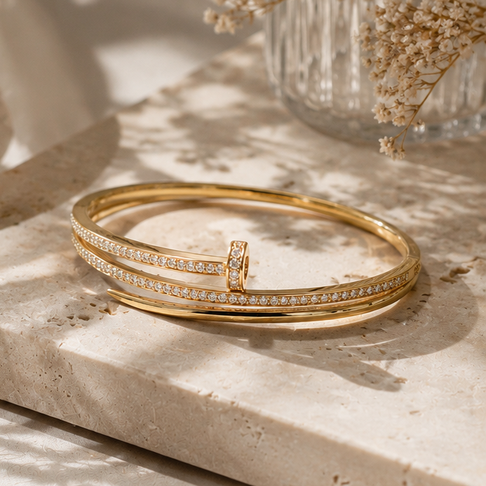 Gold bracelet with a small ring on a light stone surface with dried flowers in the background.