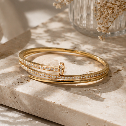 Gold bracelet with a small ring on a light stone surface with dried flowers in the background.