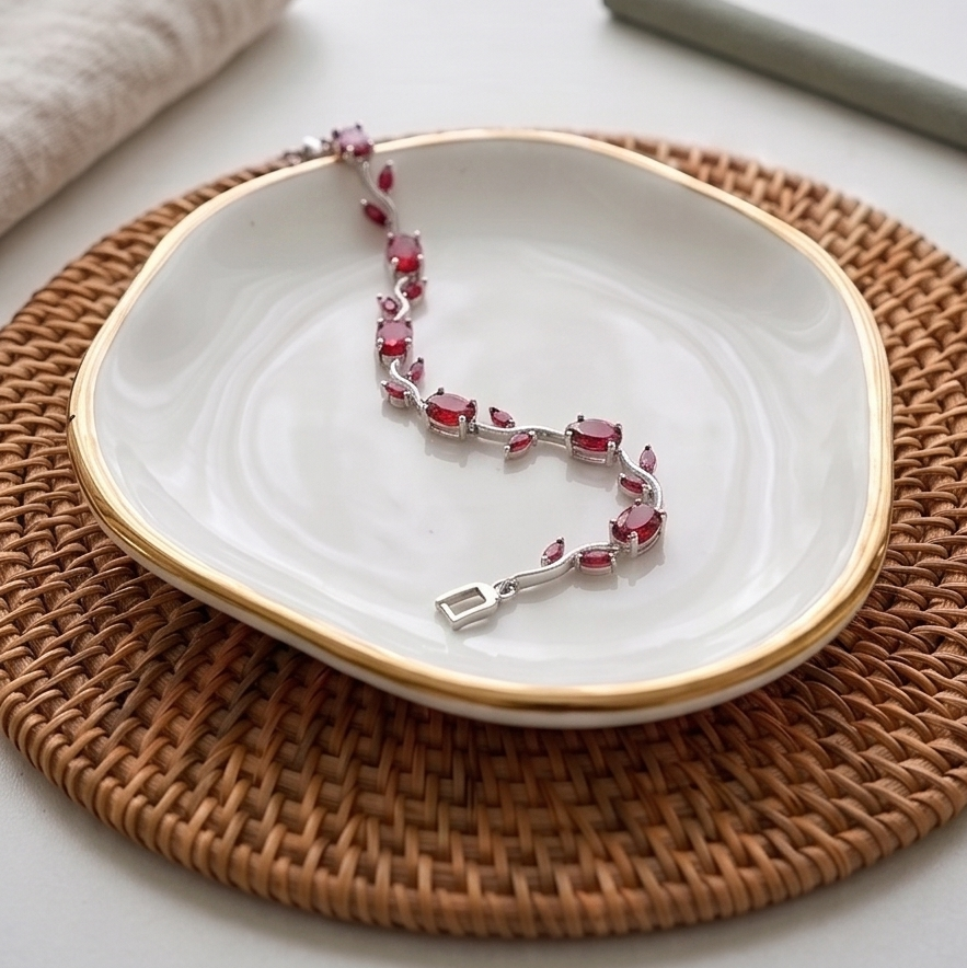 Bracelet with red stones on a white plate with gold rim, placed on a woven mat.