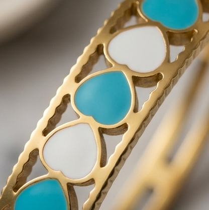 Gold bracelet with turquoise and white heart-shaped stones on a neutral background