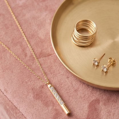 Gold necklace, rings, and earrings on a pink surface with a gold tray.