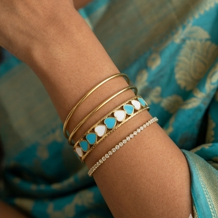 Close-up of a wrist wearing multiple gold and turquoise bracelets against a blue fabric background