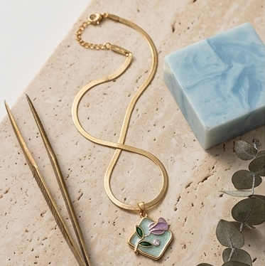 Gold necklace with a heart-shaped pendant on a stone surface with a bar of soap and eucalyptus leaves.